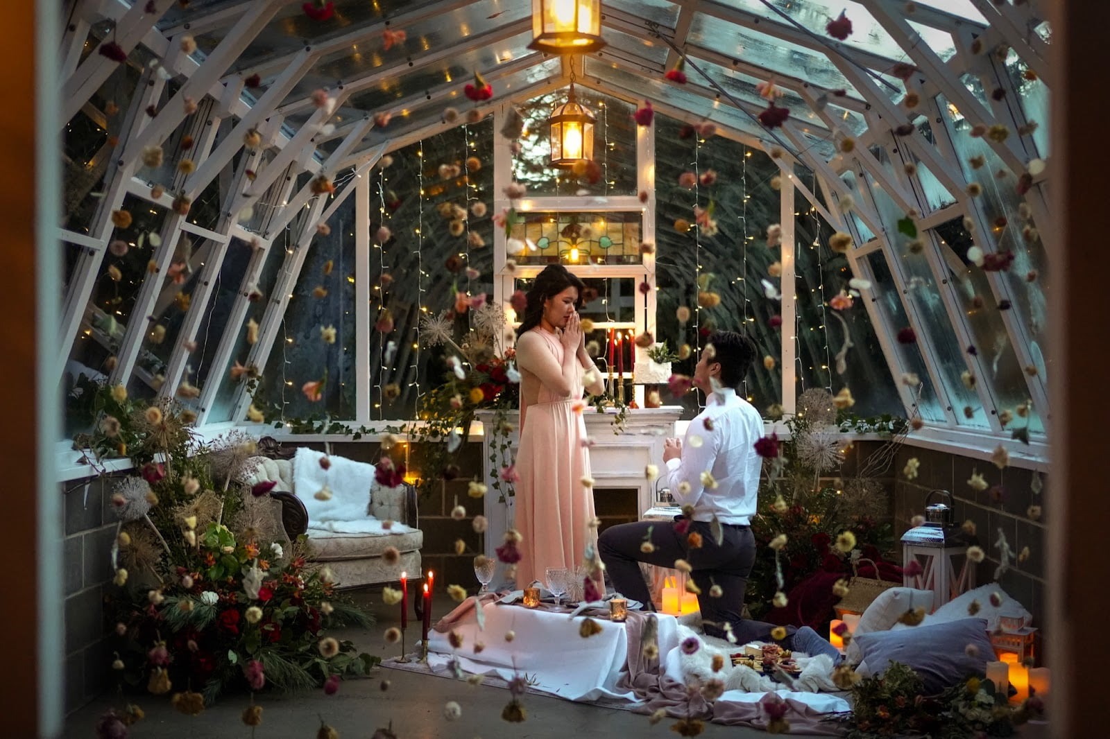 Man proposes to woman, on bended knee in beautifully decorated greenhouse at night