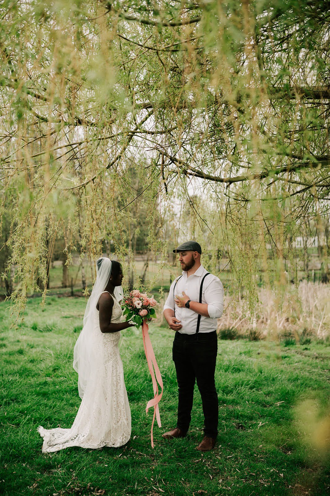 Bride holds bouquet while talking with Groom under a willow tree.