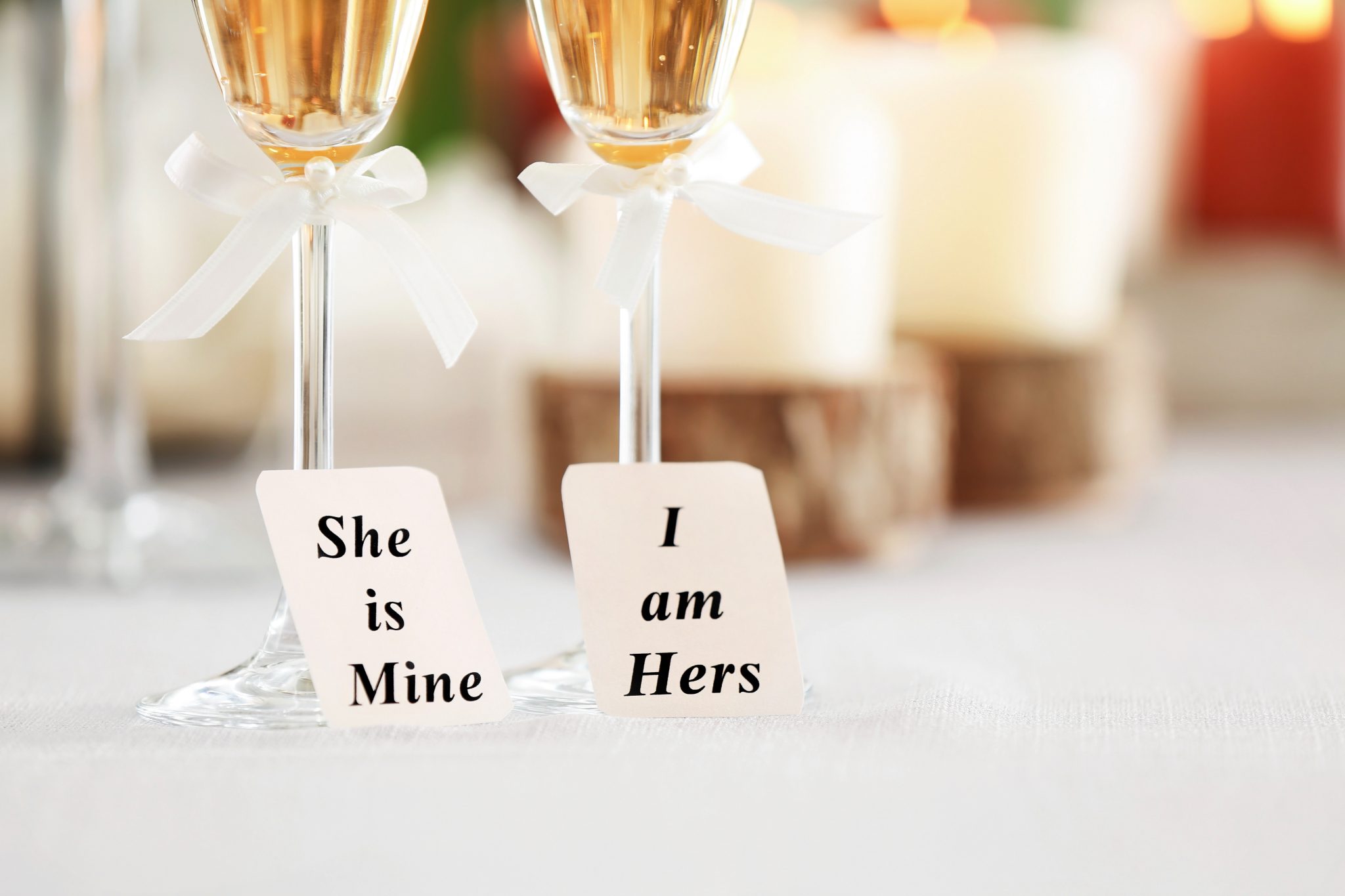 Two champagne glasses with small signs that read 'She is mine' and 'I am hers.'