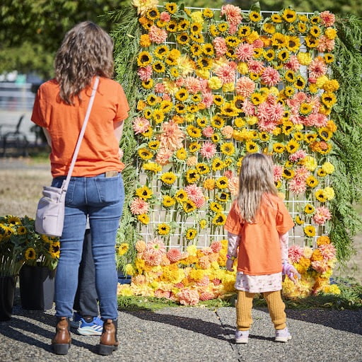 A woman and a child stand in front of a wall of yellow and orange flowers