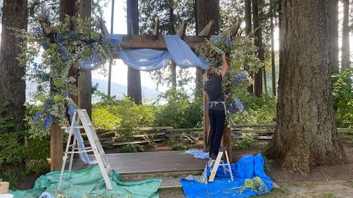 Floral designer Alexandra Richards installs floral garlands on a wooden arch